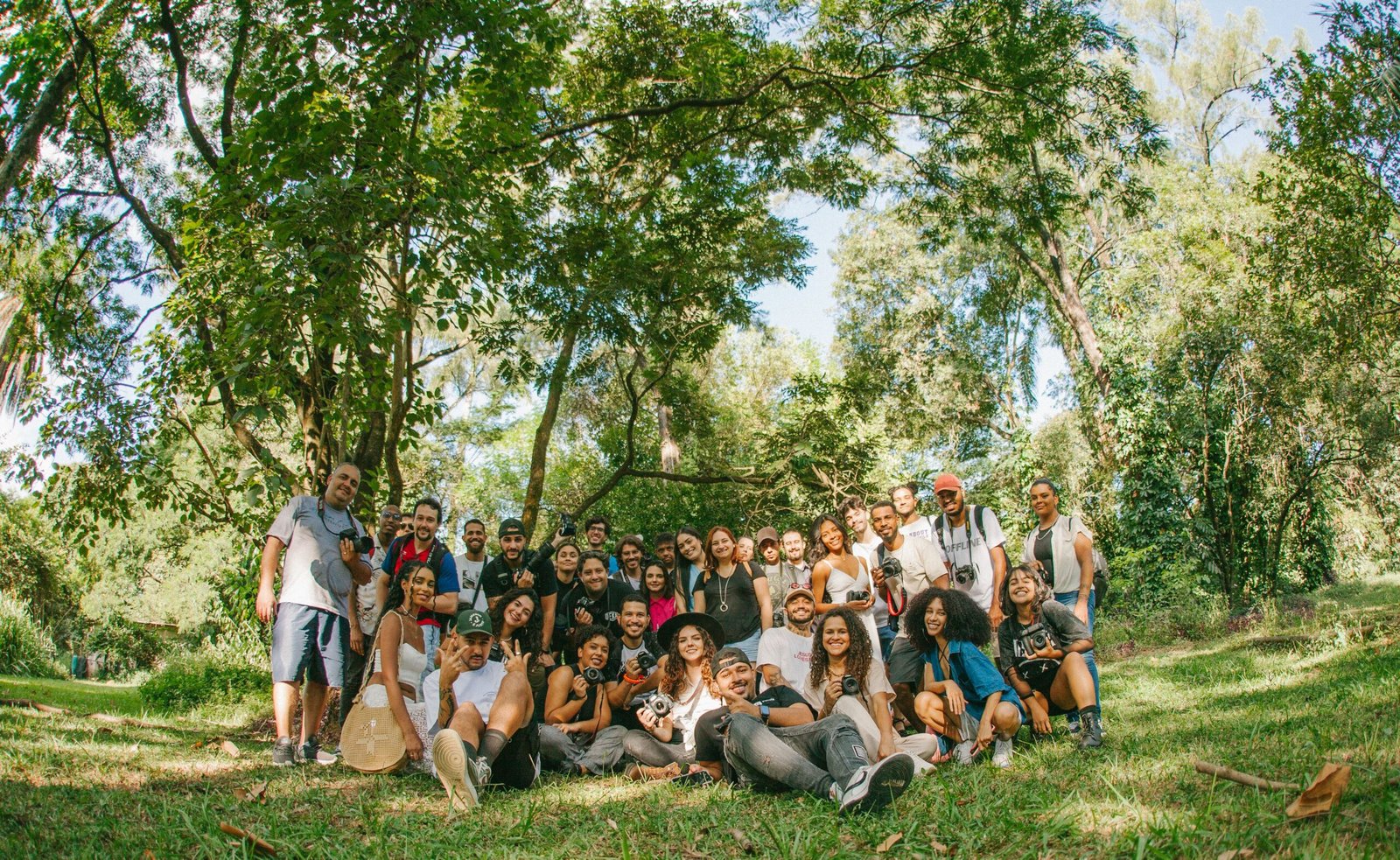 A diverse group of joyful people posing together outdoors in a sunny park setting.